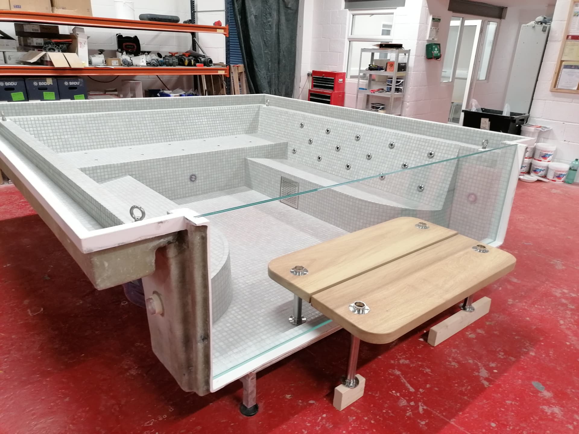 Bespoke mosaic-lined spa vessel under build, showing tile set-out, stainless jets, glass panel and teak seat